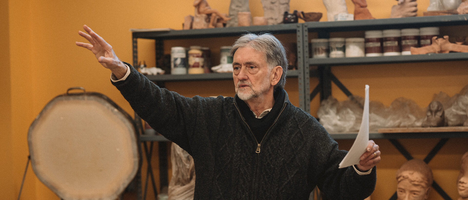 Alkion instructor Patrick Stolfo teaching clay sculpture class while standing in front of shelves displaying a variety of clay works in progress