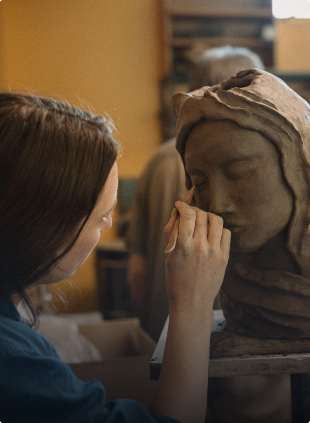 women using wooden tool for detail work on clay head sculpture.