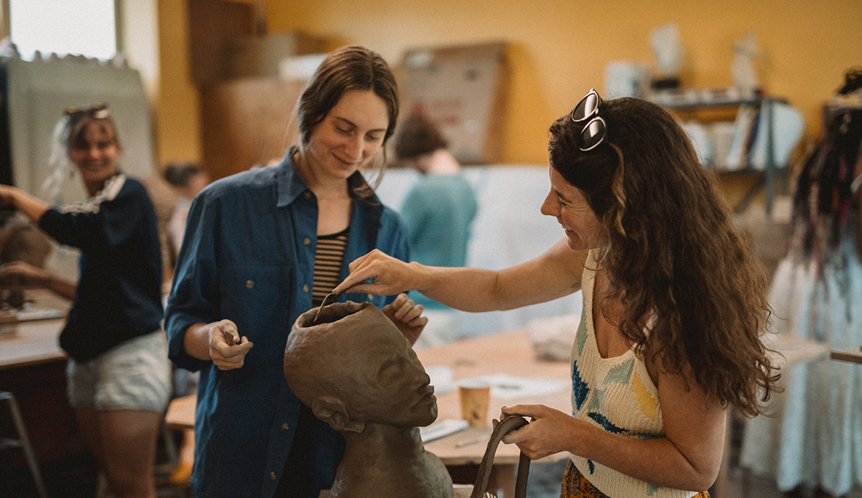 Two women sculpting clay head.